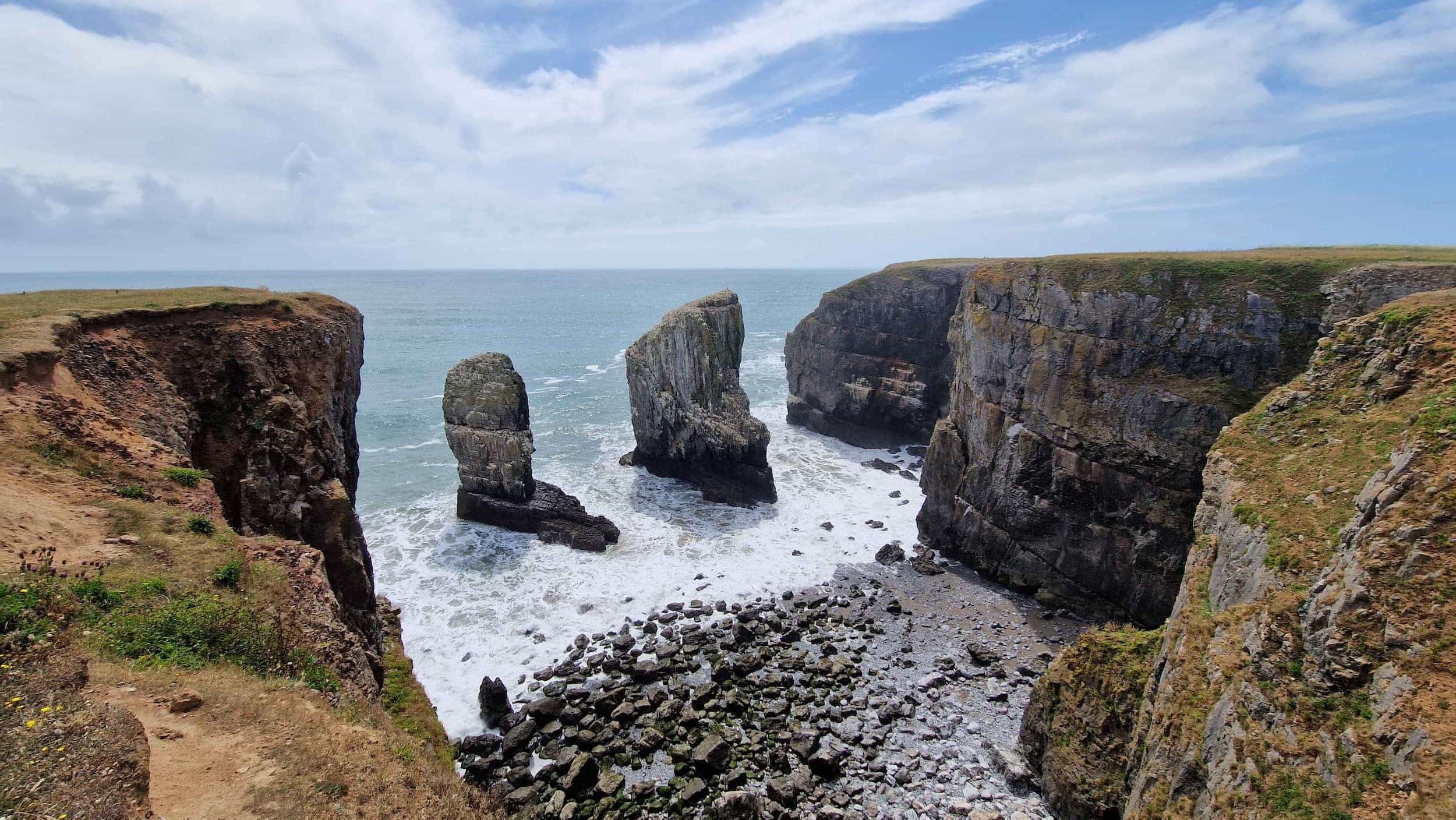 Dramatic sea cliffs with rugged rock formations jutting out of the ocean, surrounded by foamy waves and a rocky shoreline under a partly cloudy sky.